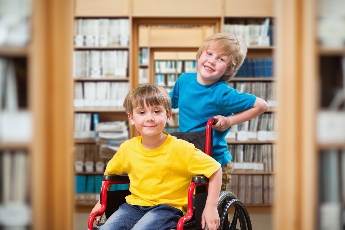 Happy boy pushing friend on wheelchair against library