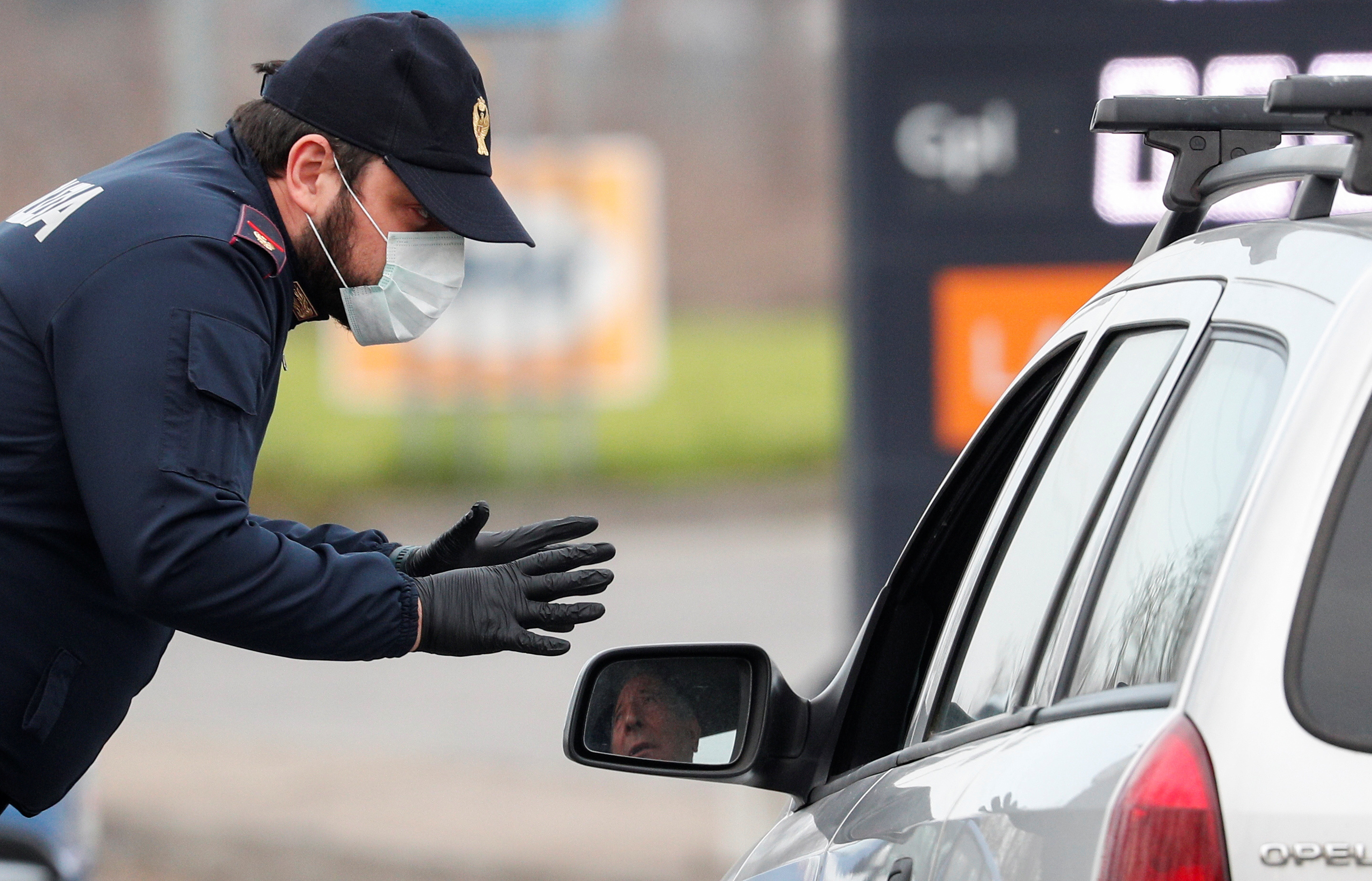 A policeman wearing a face mask warns a driver on the road between Codogno and Casalpusterlengo, which has been closed by the Italian government due to a coronavirus outbreak in northern Italy
