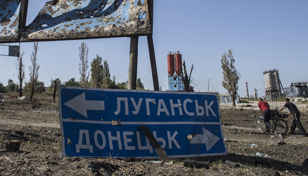 Two men push a bicycle past a direction board in the village of Lutugine just outside Luhanks