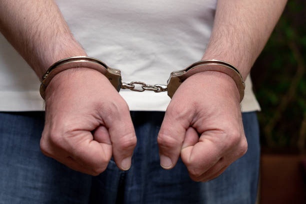 Men's hands in handcuffs. A man in a white T-shirt in handcuffs. Close-up.