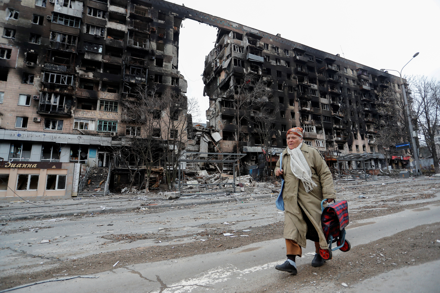 A woman walks near a destroyed building in Mariupol