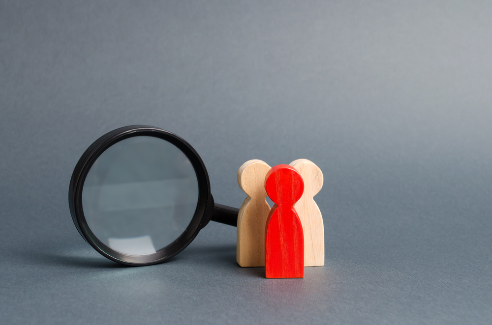 Team of wooden human figure stands near a magnifying glass on a gray background. The concept of the search for people and workers. Search for vacancies and work. Human resources, management.