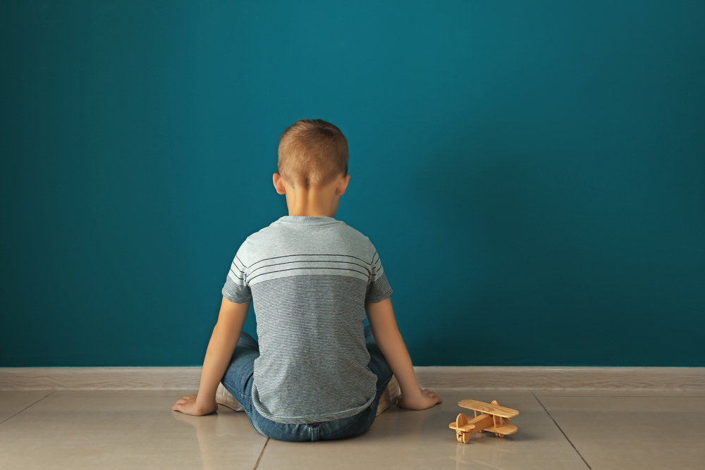 Little boy sitting near dark wall in empty room. Autism concept
