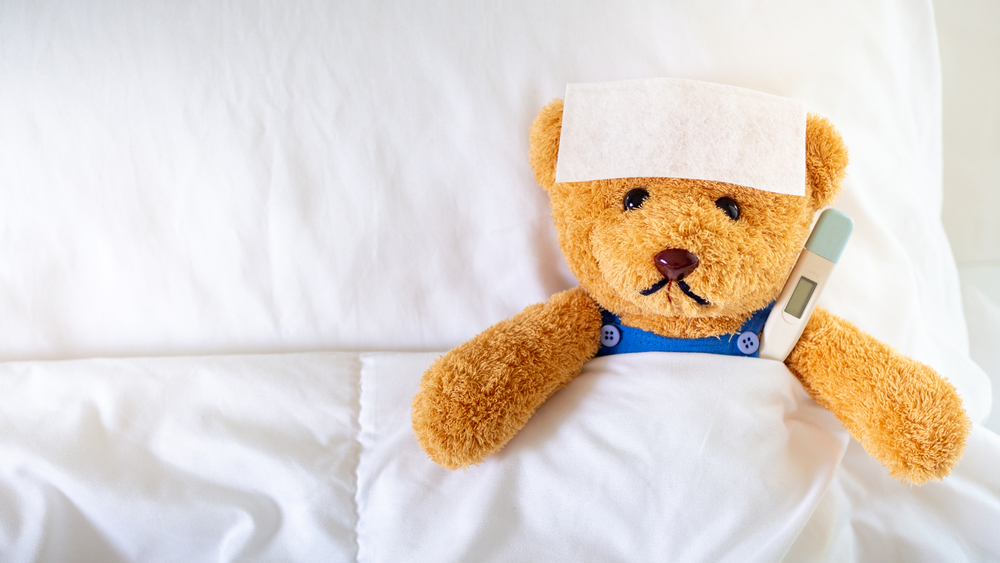 The teddy bear slept with a high fever in the bed. Together with a thermometer.