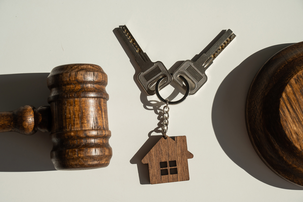 Keys with a keychain in the shape of a house and a judge's gavel on a white background.