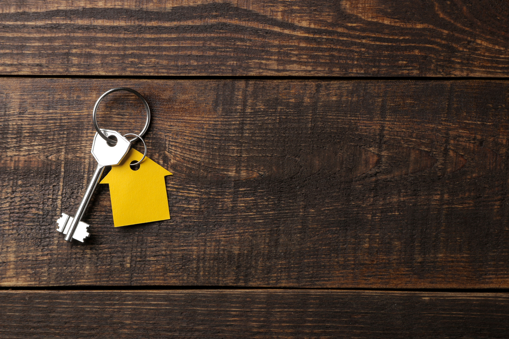 The concept of buying a home. Keys with keychain house on a brown wooden background. view from above. with space for inscription