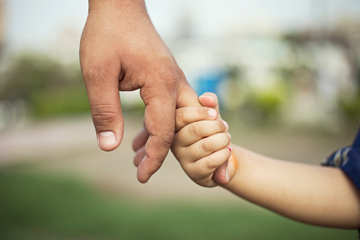 Father holding hands of his little daughter at park
